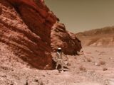 An astronaut in a spacesuit explores a barren, eroded desert, resembling Martian terrain.